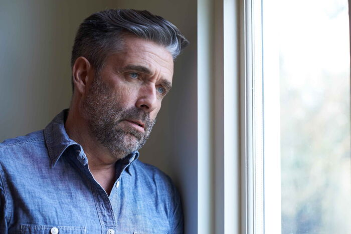 Ein Mann schaut ängstlich und trübsinnig aus dem geschlossenen Fenster.